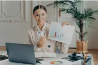 Bookkeeper on SAP HANA 19 Person in a beige suit presenting a chart next to a laptop on a desk.
