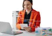 Person in orange jacket using a tablet at a desk with laptop and color swatches.