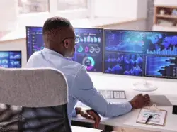 Man in office analyzing data on multiple computer screens.