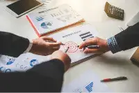 Bookkeeper on SAP HANA 9 Professionals discussing charts and data with a target graphic on a desk.
