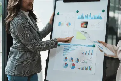 Woman presenting business graphs and charts on a whiteboard.